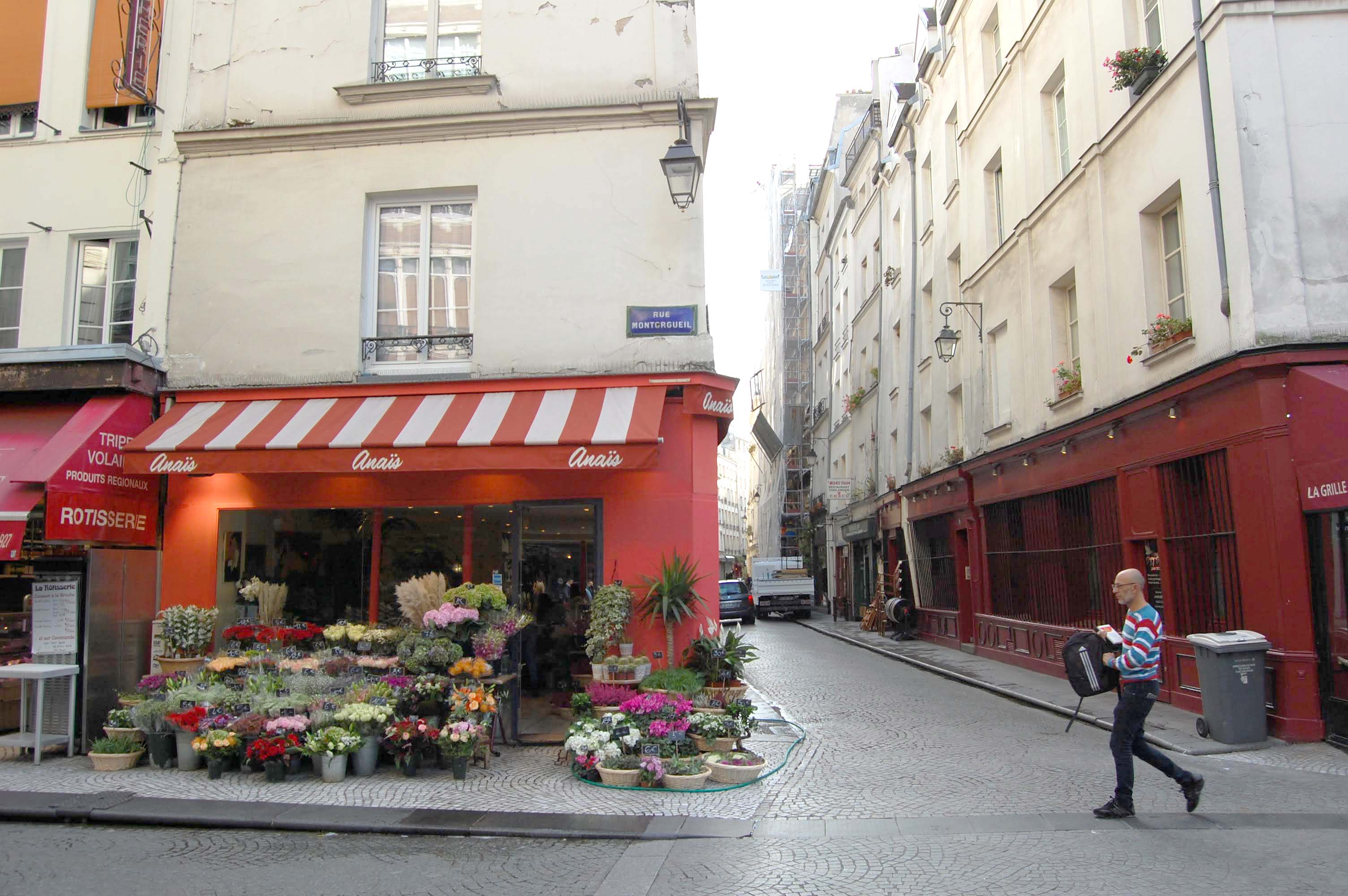 Pedestrian walking past flower shop display on Rue Montorgueil, showcasing local specialty shopping